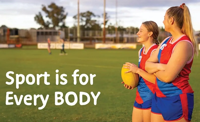 Two female Aussie rules players stand on an oval in their red and blue footy uniforms