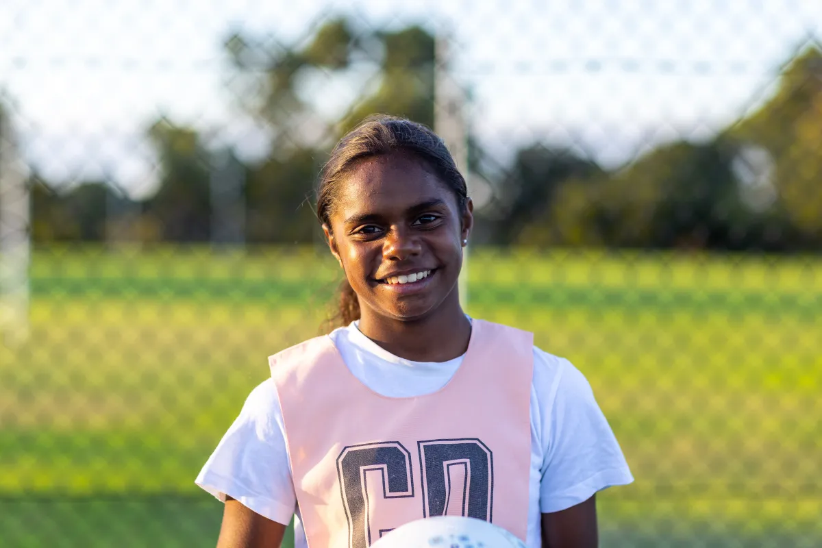 Australian female Indigenous netball player, smiles in a pink Goal Defence (GD) bib, holding a netball
