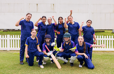 Girls cricket team in navy blue uniforms cheering together