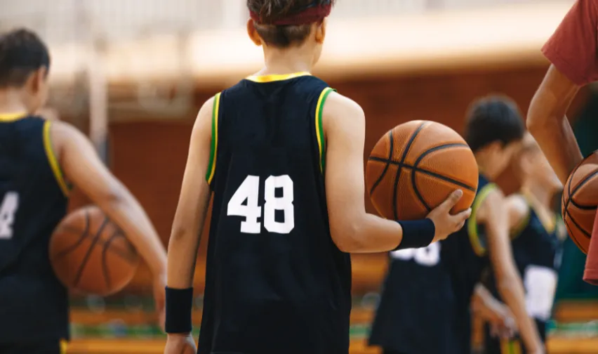 A young basketballer holds a basketball in hand with number 48 in white on the back of their black singlet