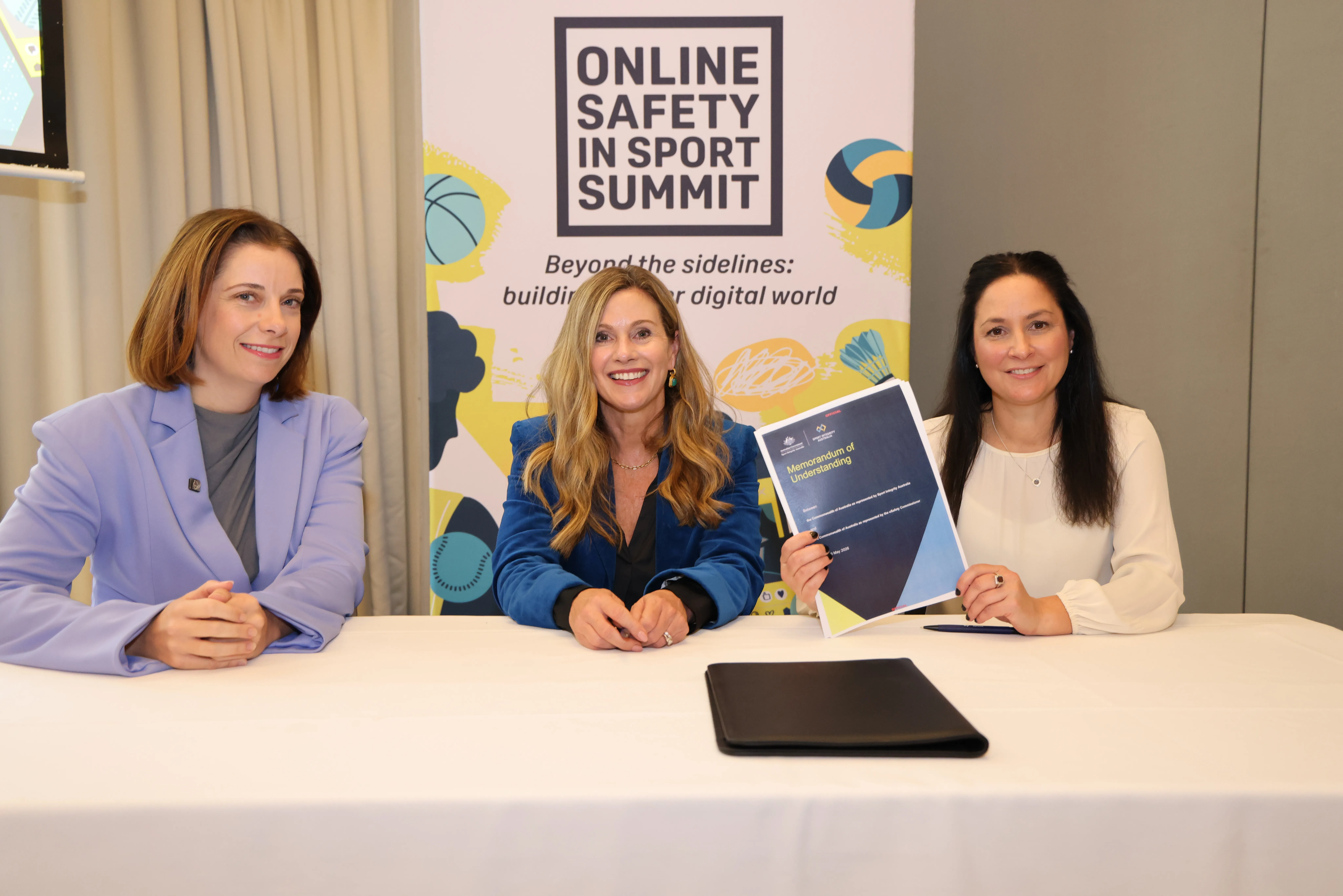 The Hon Anika Wells MP, eSafety Commissioner Julie Inman Grant PSM and Dr Sarah Benson PSM with a MoU sitting in front of the Online Safety in Sport Summit banner