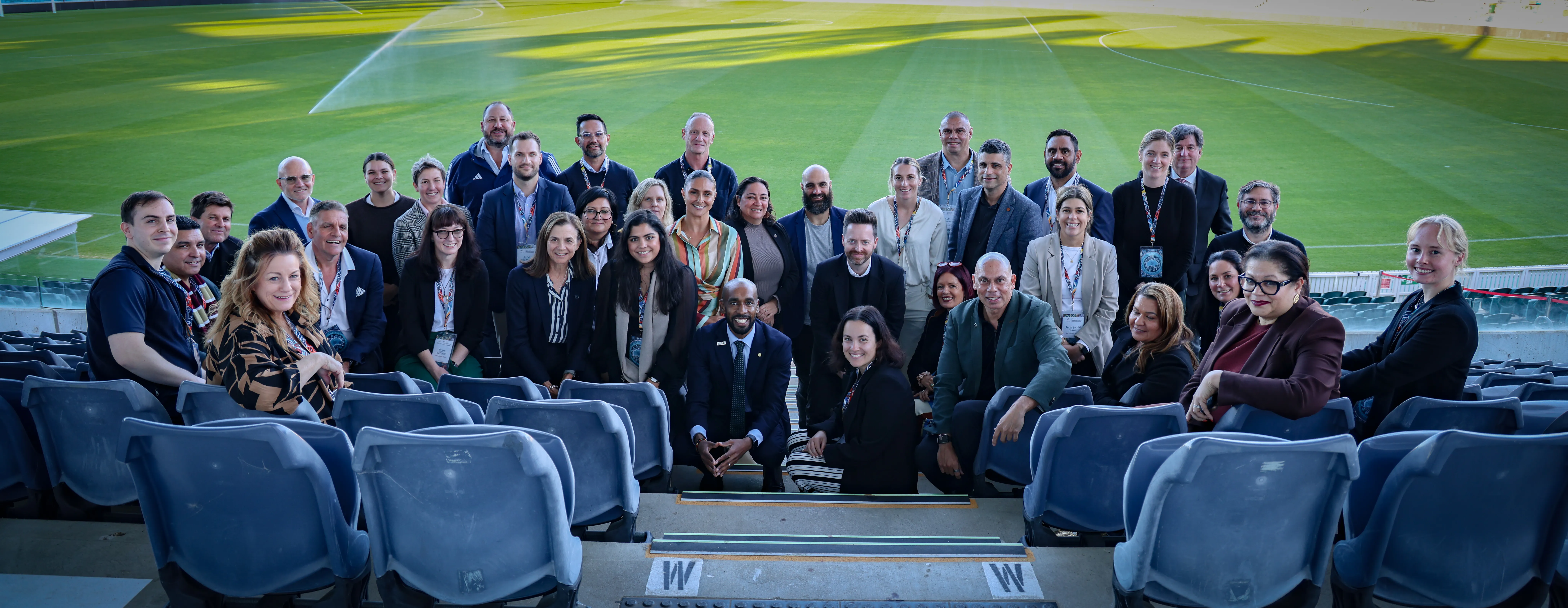 Group photo of attendees of the Racism and Racial Discrimination in Sport Roundtable in the stands of a football ground