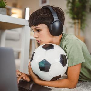 online safety boy holding soccer ball looking at laptop with headphones on