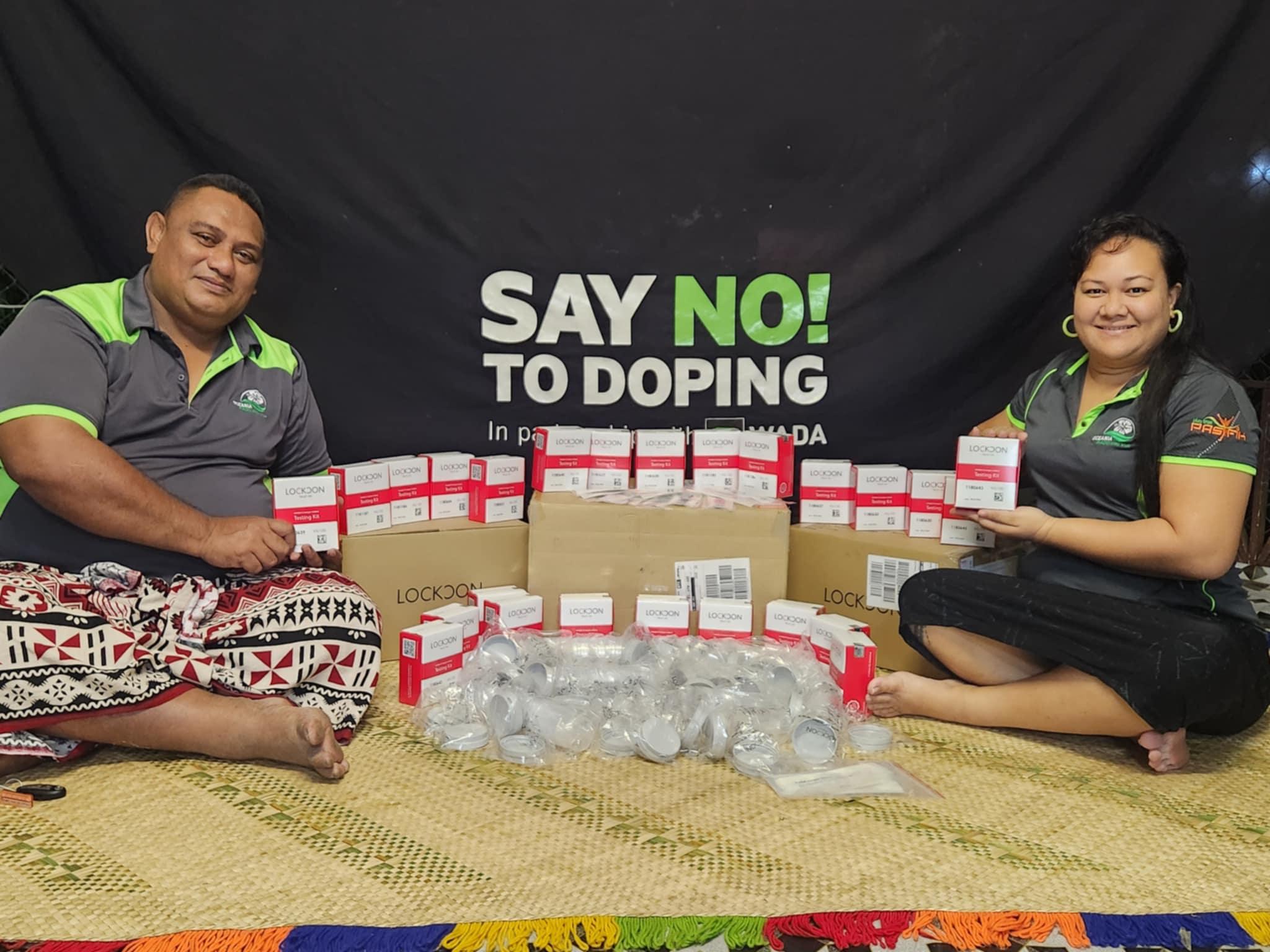Samoa Medical and Anti-Doping Agency team members sit in front of a banner saying 'say no to doping' and display anti-doping test devices