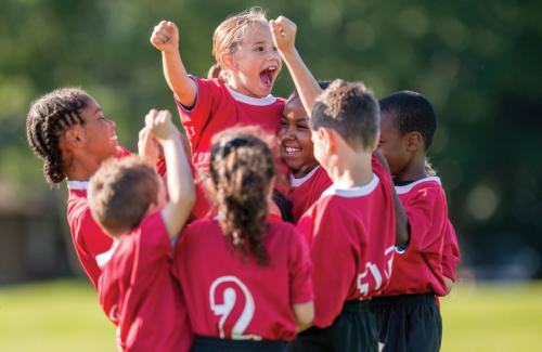 A team of young children in a soccer team with red jerseys huddle and celebrate together