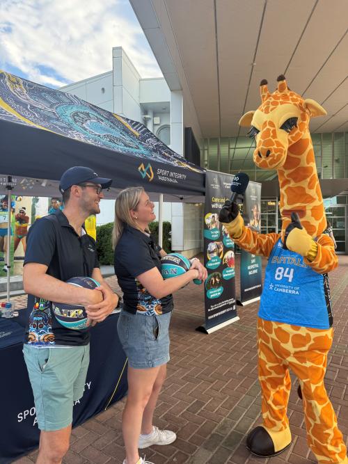 Sport Integrity Australia staff with Cappie the giraffe holding a microphone