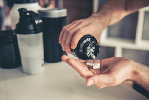 A person takes a sport supplement from a container with a protein shaker in the background