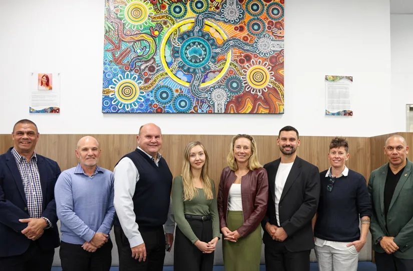 The 8 members of the Culture and Safety Advisory Committee standing in front of First Nations artwork