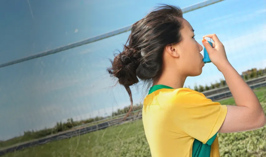 Female athlete in yellow shirt using an asthma puffer on a soccer field
