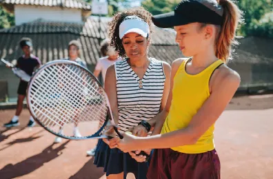 Female tennis instructor showing a girl how to hold a tennis racquet