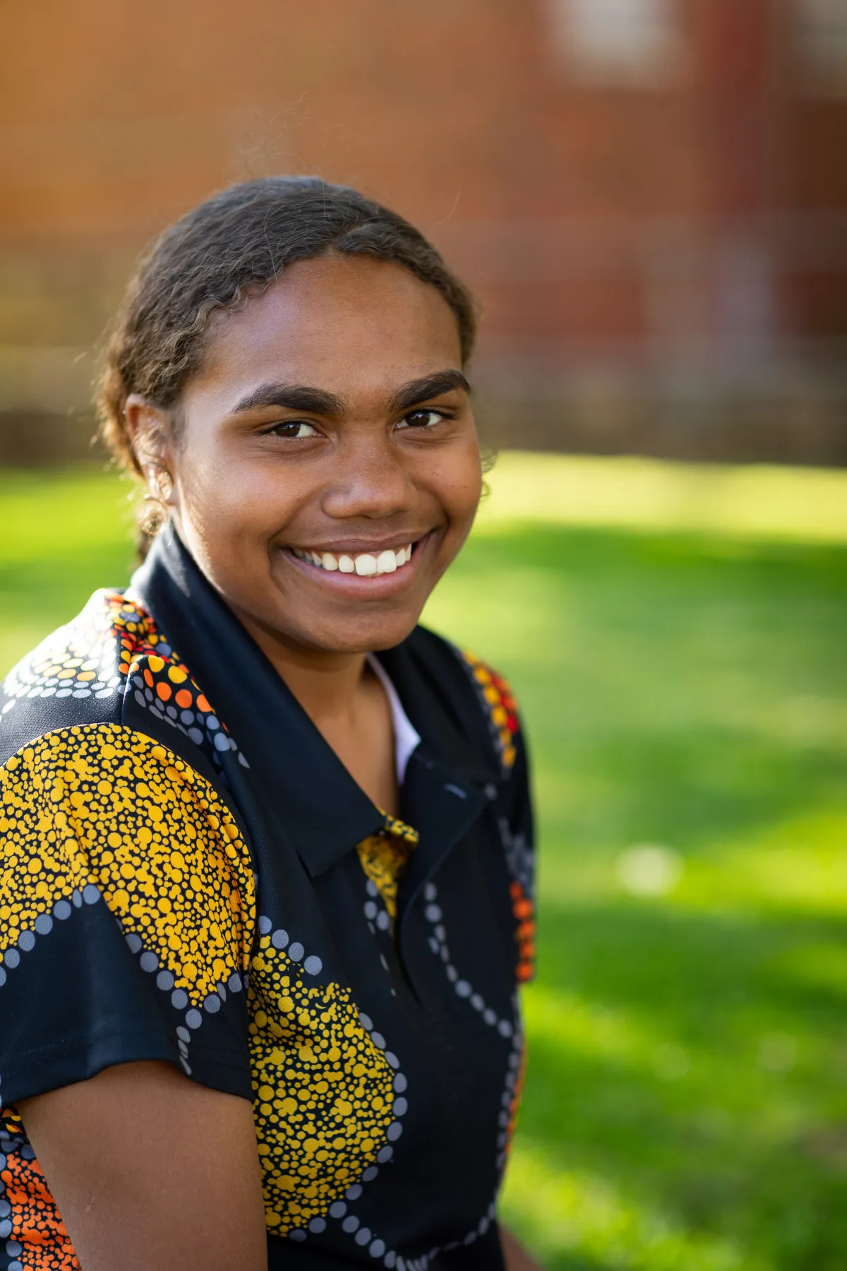 Australian First Nations woman wearing an Indigenous themed shirt, smiles at the camera