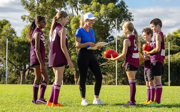 A female football coach gathers young people in the team on the field - Positive Behaviours in Sport Study media statement