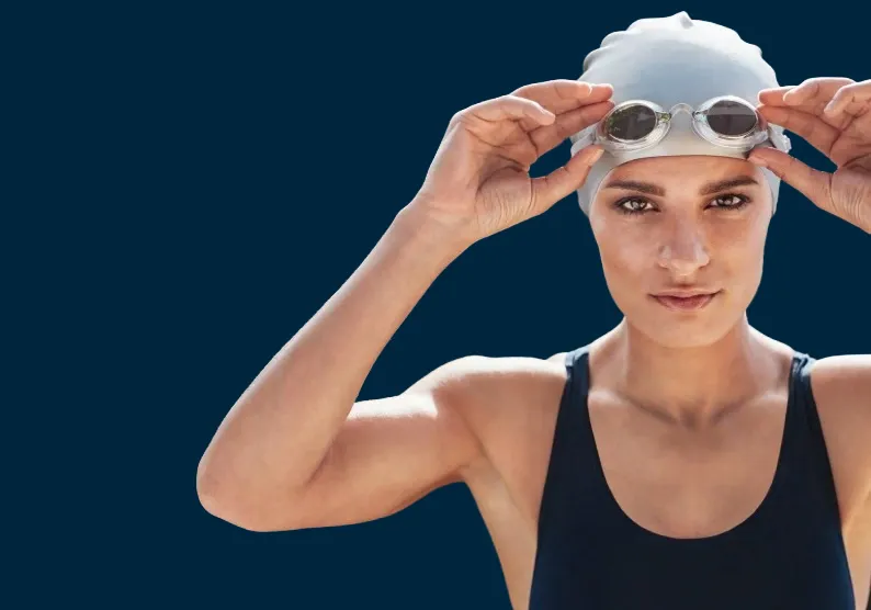 Swimmer in black swimwear and silver swimming cap, gets ready to place goggles on