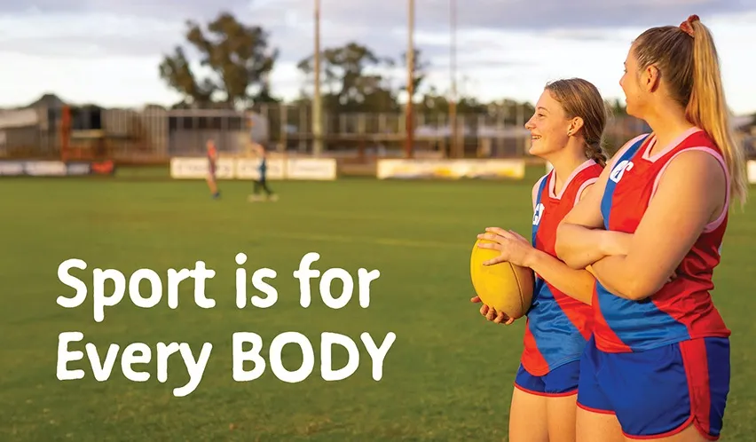 Two female Aussie rules players stand on an oval in their red and blue footy uniforms