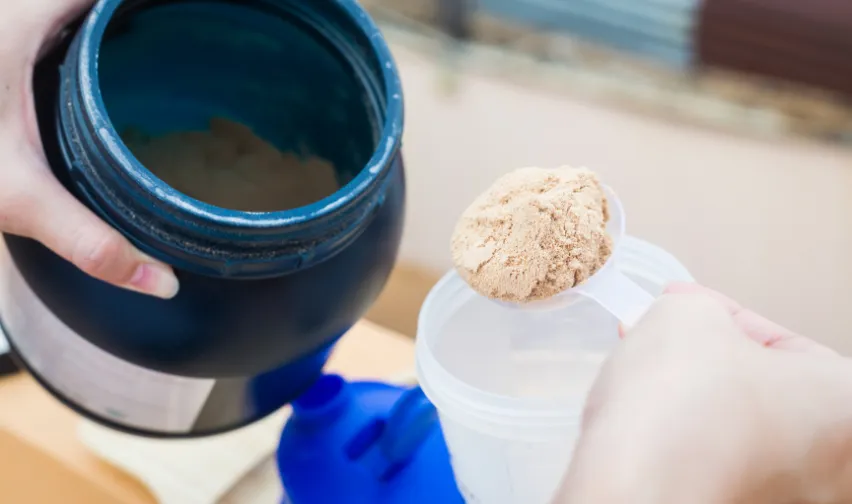 person holding a supplement tub and scooping out supplement powder
