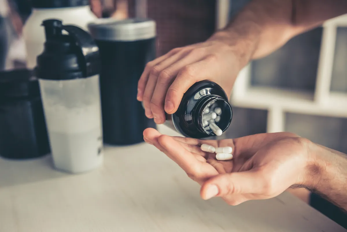 A person takes a sport supplement from a container with a protein shaker in the background