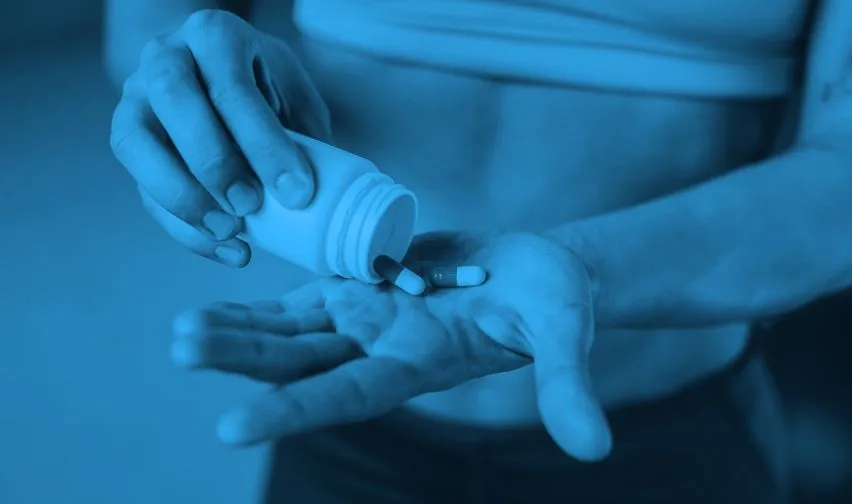 An athlete pours pills from a container into the palm of their hand